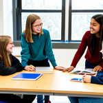 A diverse group of middle school students, fully clothed in modest, school-appropriate attire, actively collaborating around a large table in a bright, modern school maker-space. They are engaged in a hands-on interdisciplinary project, using various educational materials and technology. Students are discussing, pointing, and sharing ideas with genuine engagement. This image promotes a professional, family-friendly atmosphere of collaborative learning. safe for work, appropriate content, perfect anatomy, correct proportions, natural pose, well-formed hands, proper finger count, natural body proportions, professional photography, high quality.